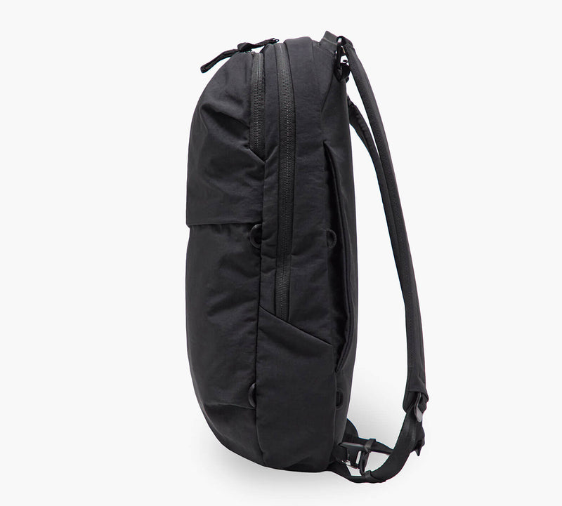 Black slim backpack in side profile with top zipper, padded shoulder straps and a front pocket.