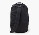 Black single-strap sling backpack shown from rear, padded strap and top carry handle.