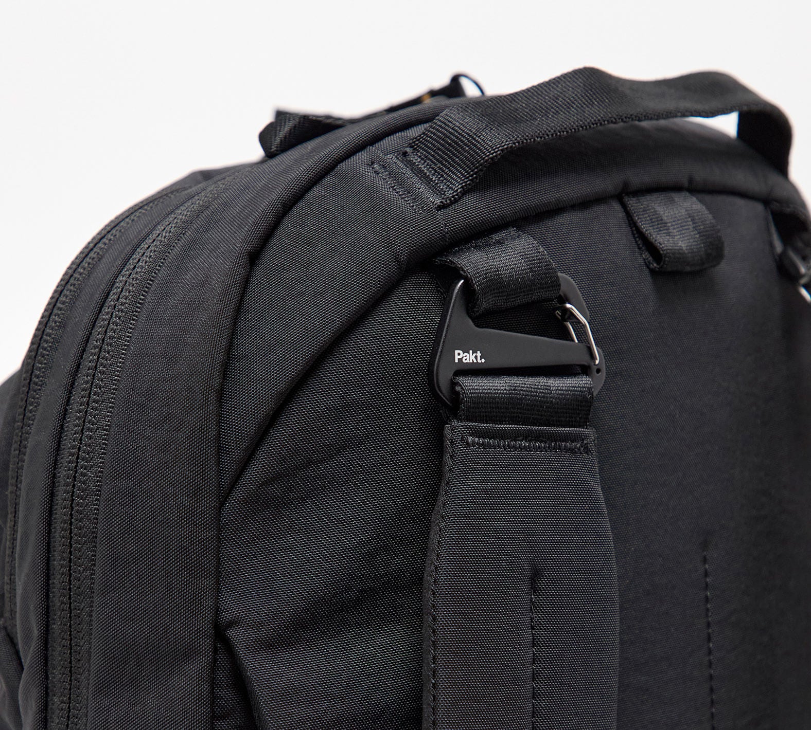 Close-up of MODE Convertible Bag 14L back showing black padded detachable shoulder strap secured by a metal clip stamped with Pakt on a white background