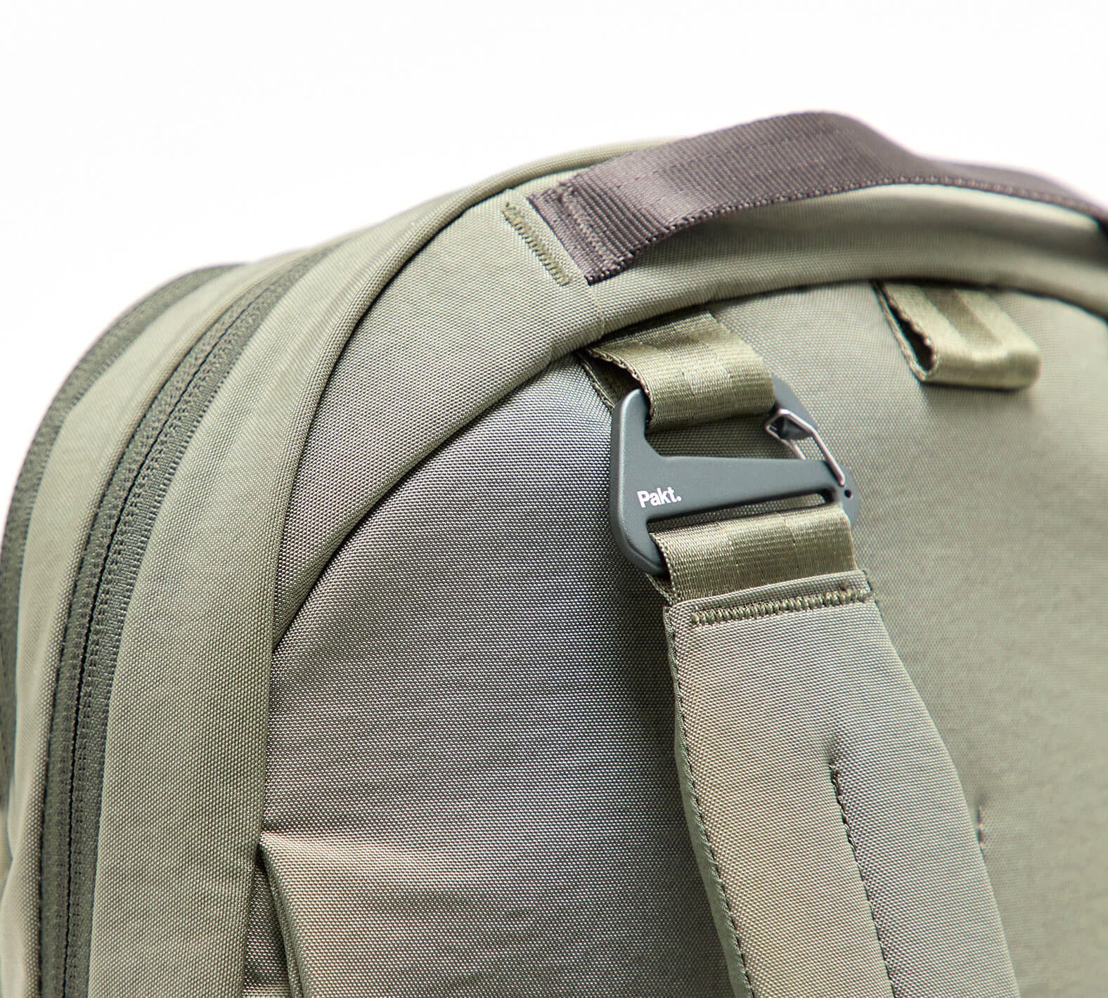 Close-up of olive-green strap and metal carabiner-style clip stamped 'Pakt.' on a convertible bag