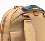 Rear shoulder strap and metal hardware of a tan backpack, showing padded handle and zipper seam.