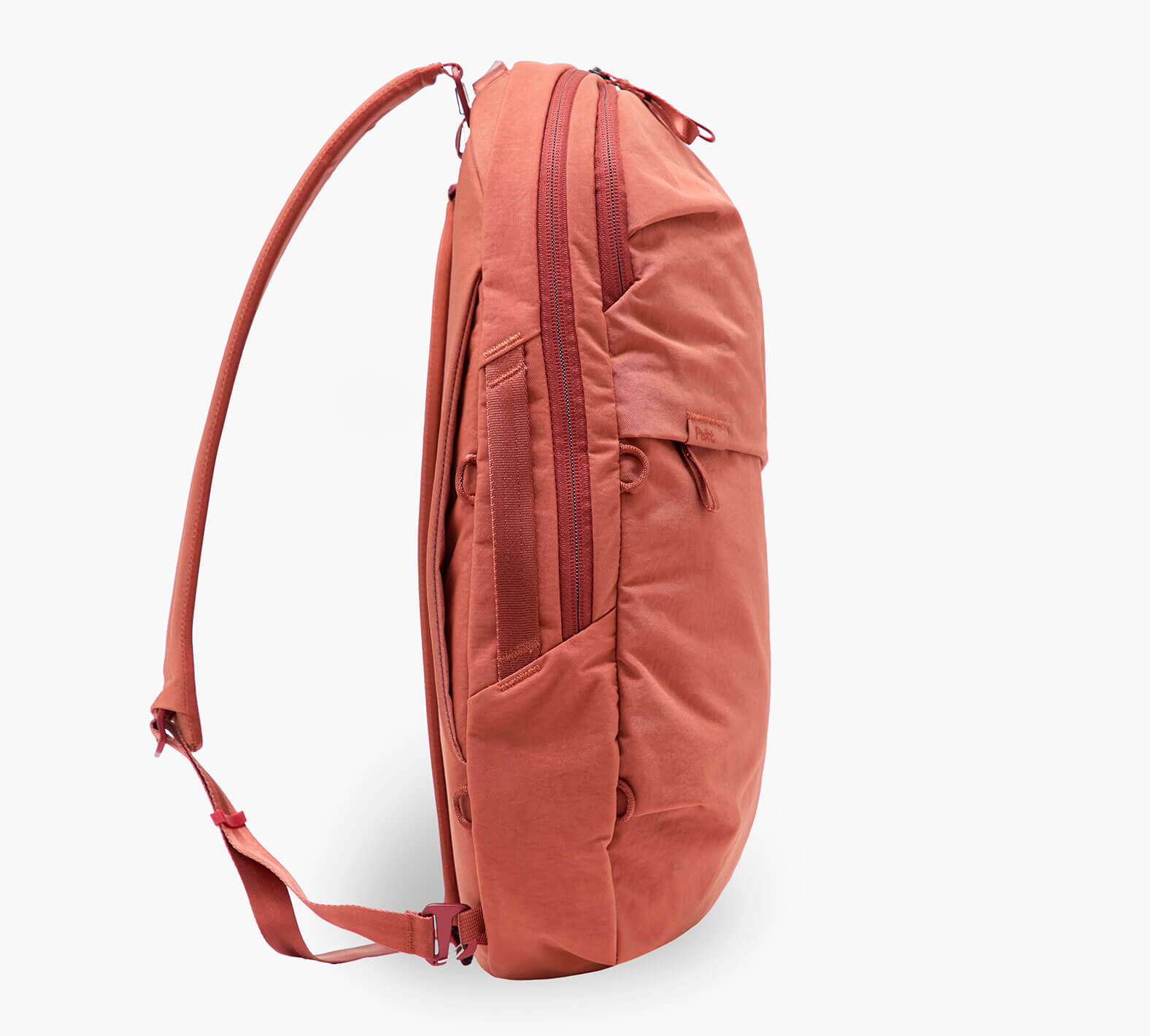 Coral-red daypack, side view showing zippered compartment and padded shoulder strap.