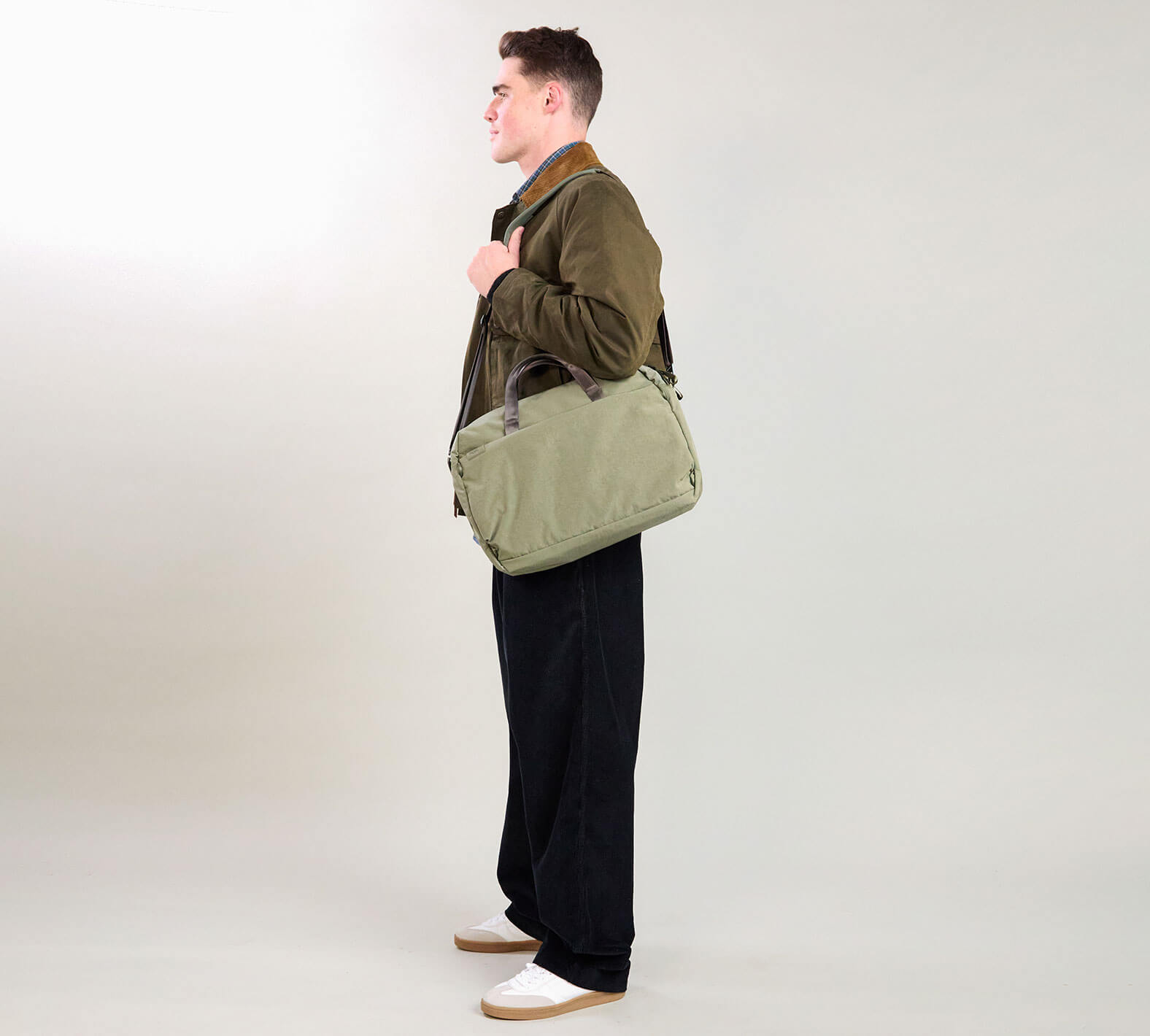 Profile view of MODE Shoulder Bag 12L in cypress showing shoulder strap and top carry handles on a light gray background