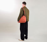 Person viewed from behind wearing an olive jacket and black wide-leg trousers, carrying a coral shoulder bag