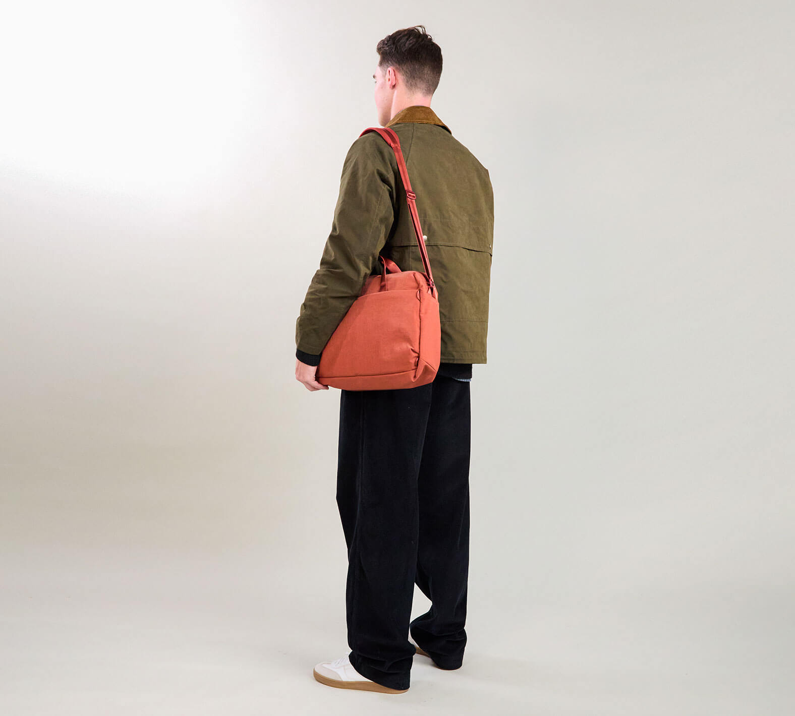 Person viewed from behind wearing an olive jacket and black wide-leg trousers, carrying a coral shoulder bag
