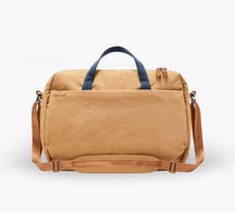 Tan canvas weekender duffel with navy top handles, adjustable tan shoulder strap, and front slip pocket.