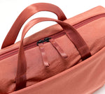 Rust-colored soft fabric bag with front pocket, top carry handles and twin zipper pulls.