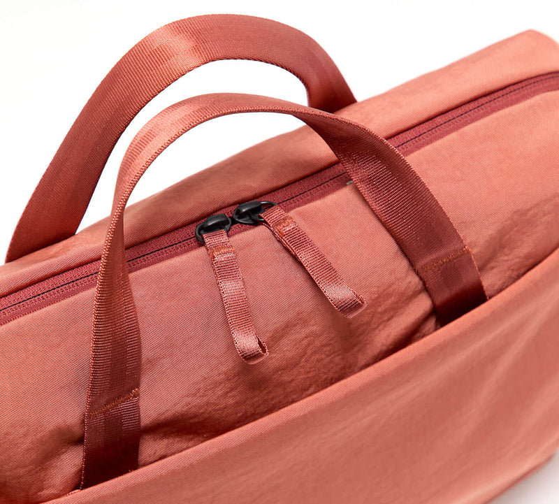 Rust-colored soft fabric bag with front pocket, top carry handles and twin zipper pulls.