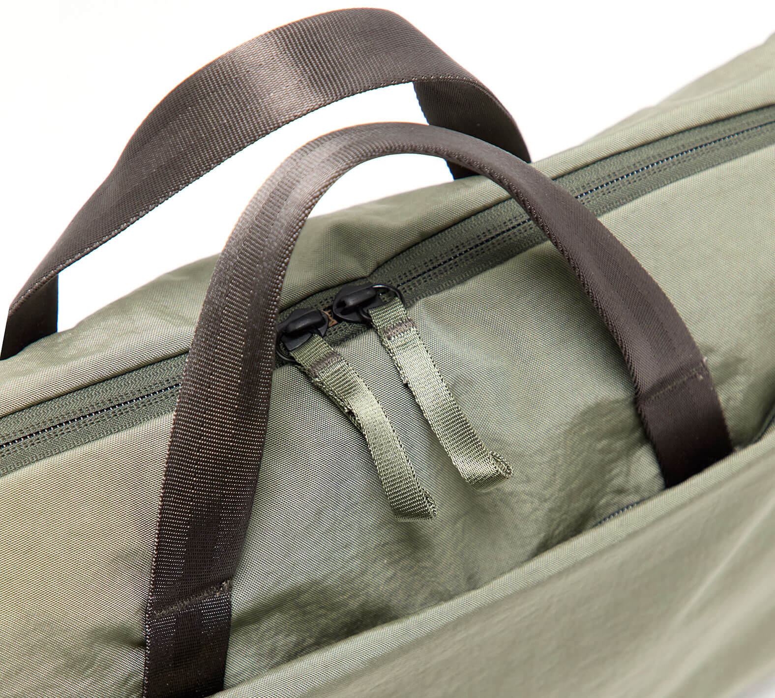 Close-up of MODE Shoulder Bag 12L showing top handles and dual zipper pulls on cypress fabric with white background