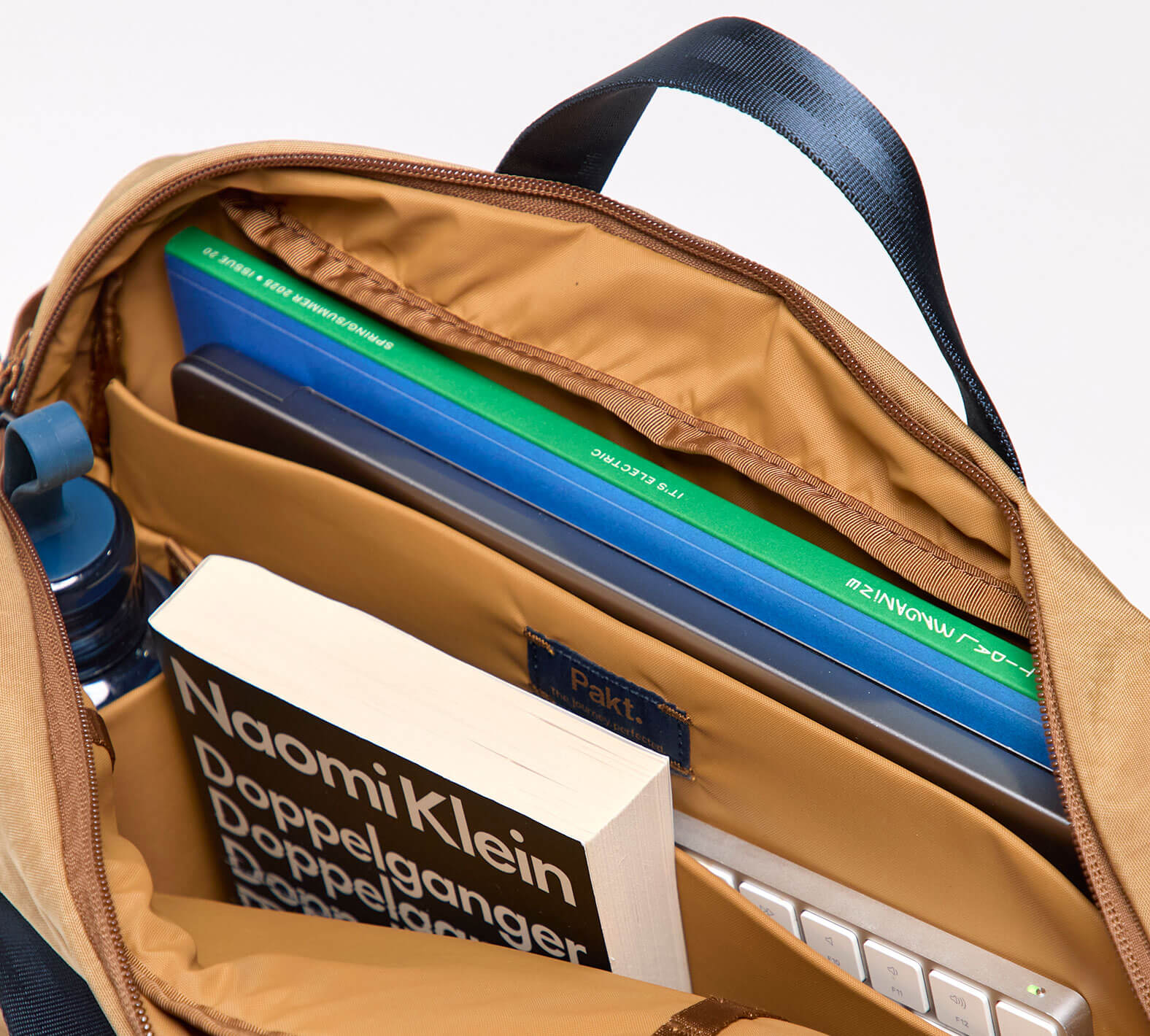 Top-down view of MODE Shoulder Bag 12L in Mojave showcasing padded laptop sleeve, internal organizer pockets, and water bottle sleeve on white background