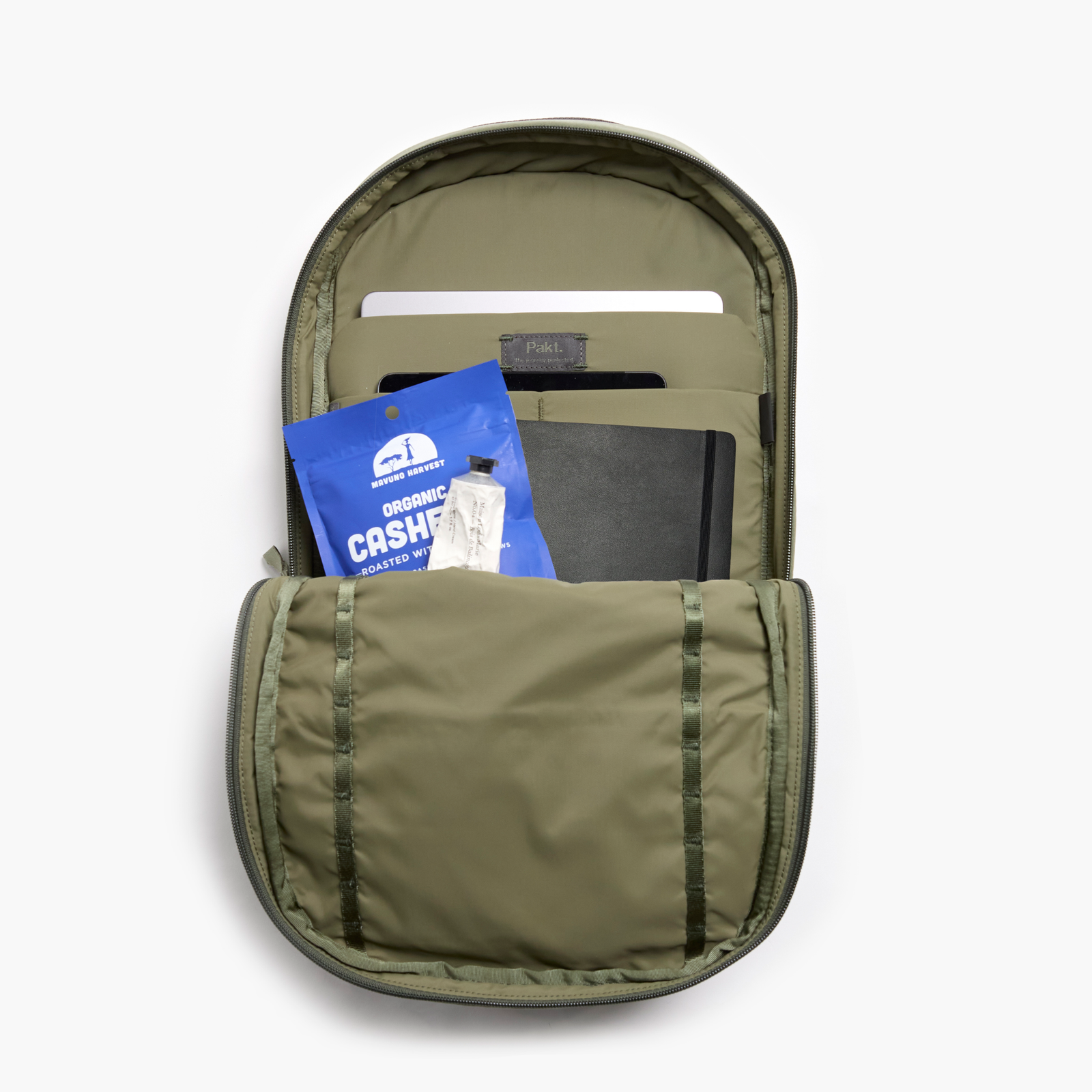 Pakt backpack interior with laptop sleeve, notebook and blue MAVUNO HARVEST ORGANIC CASHEW packet labeled ROASTED WITH.