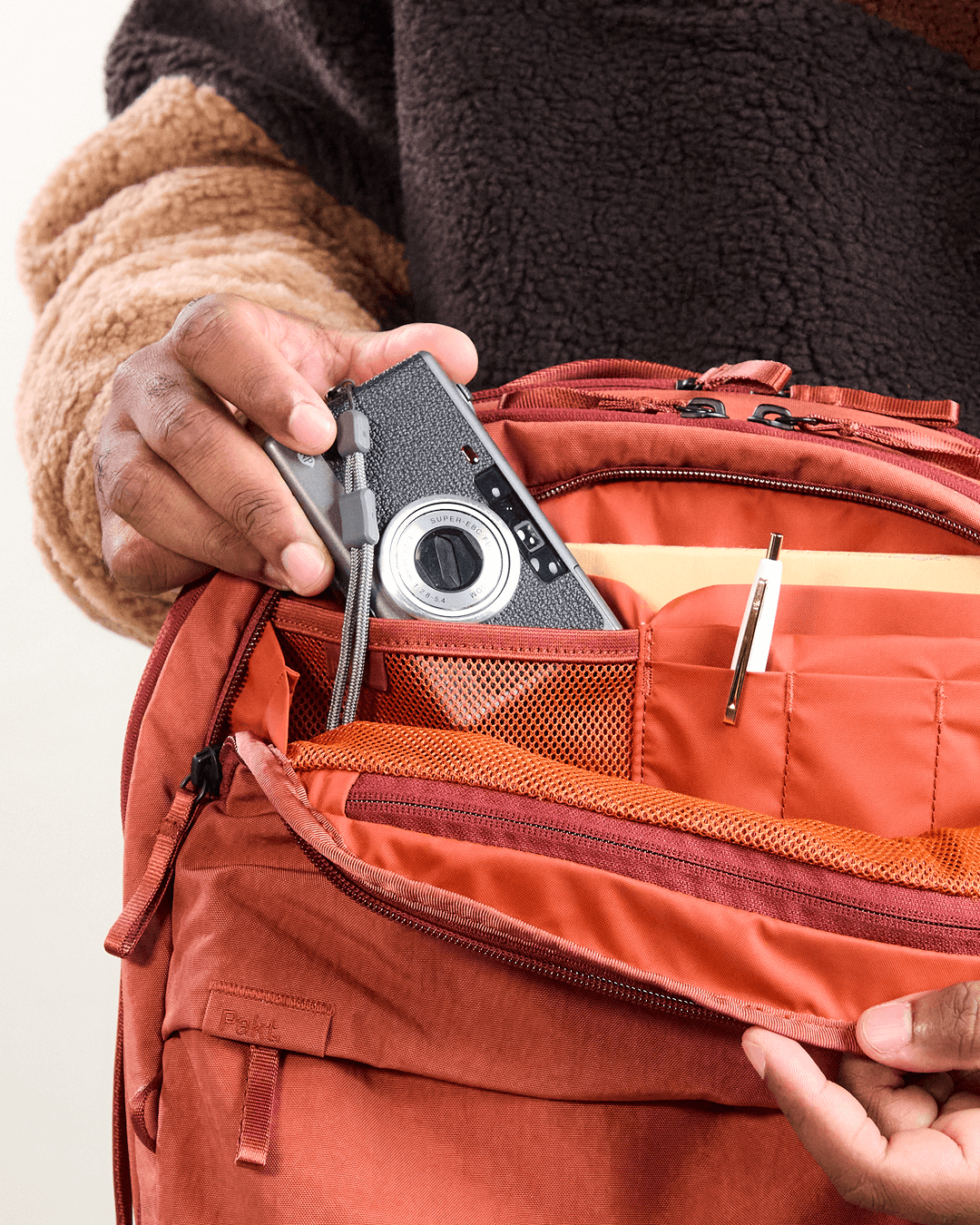 Close-up of MODE Backpack 22L in Sumac showing open admin pocket with mesh organizer, pen slots, and camera placed inside