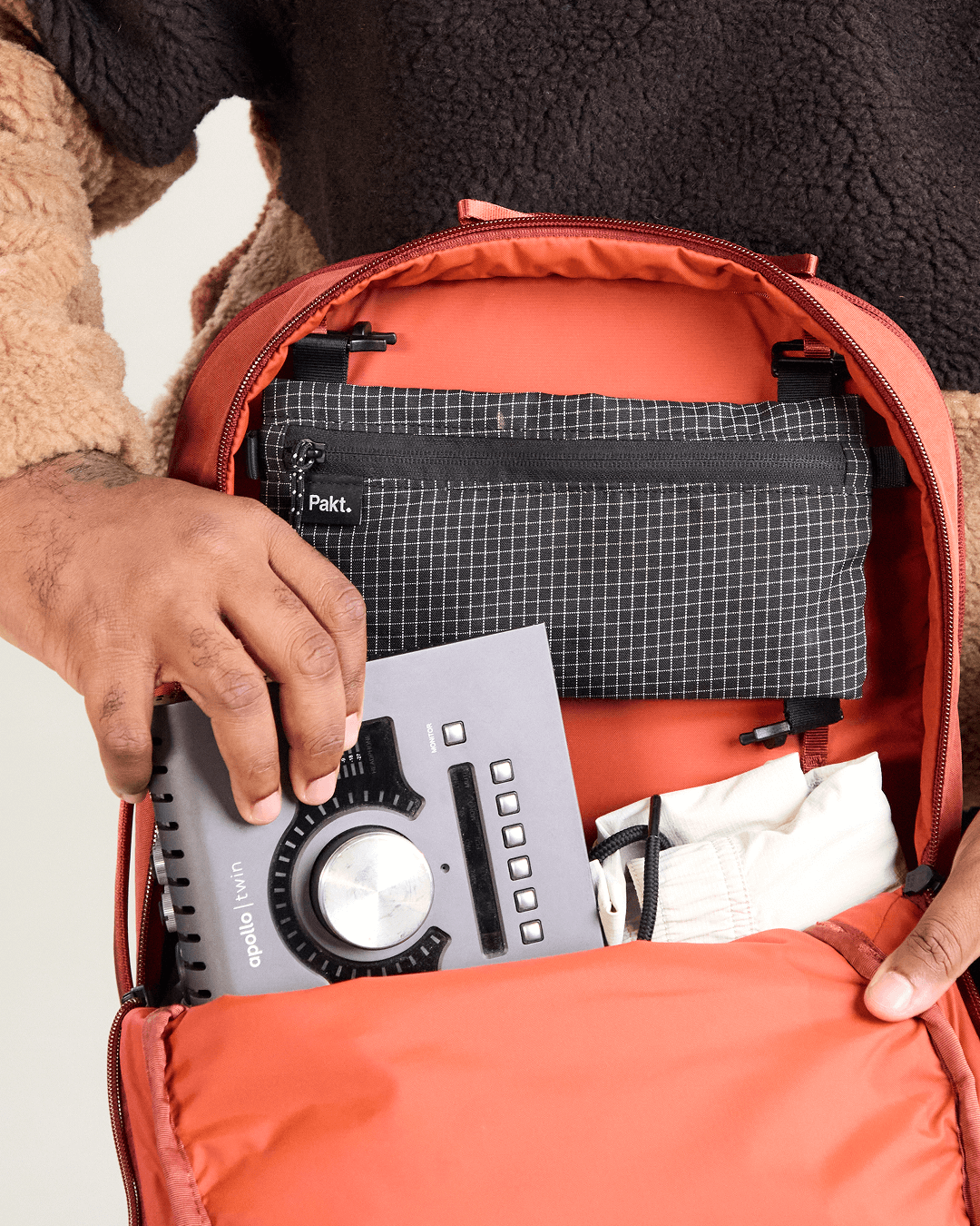 Open-front view of MODE Backpack 22L in sumac showing internal zip pocket, padded laptop sleeve, and hands placing gear