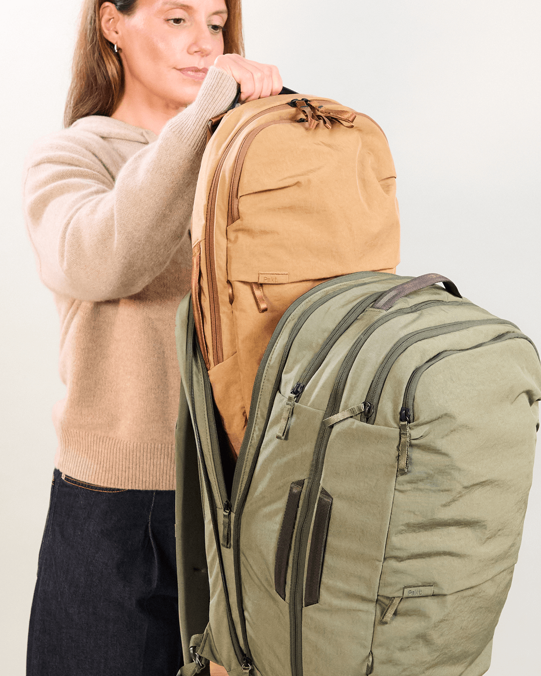 Woman placing tan Pakt daypack into open olive-green travel backpack