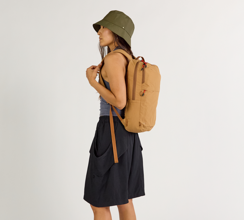 Person wearing a Mojave Stash Backpack and green bucket hat on a plain background
