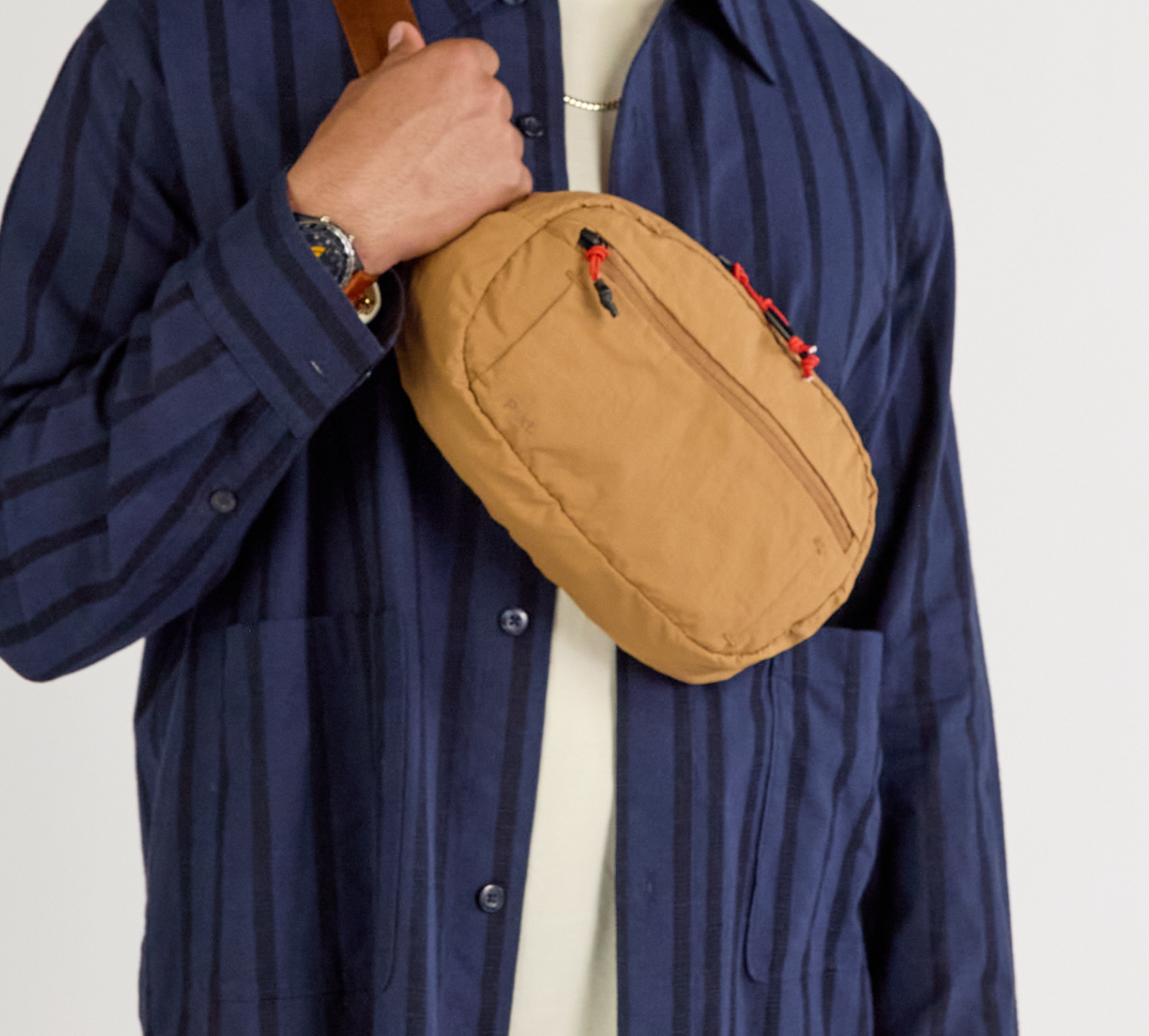 A model wearing a blue shirt with the Stash Sling in Mojave worn over.