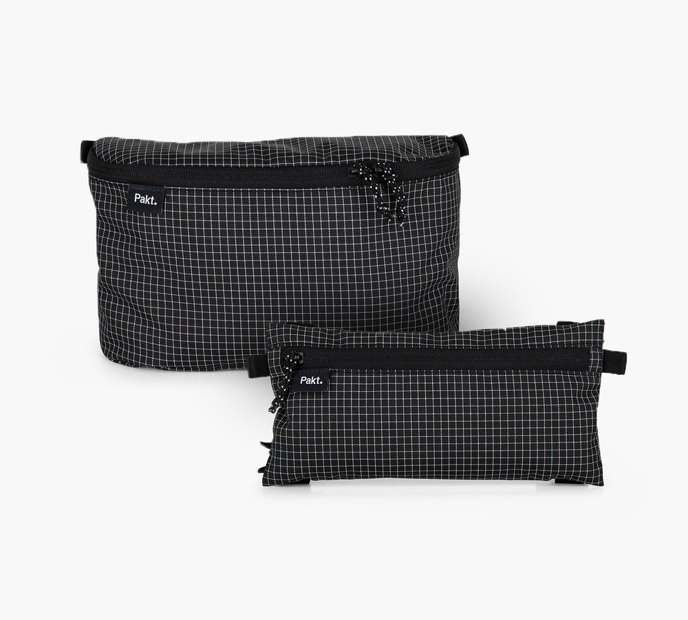 Front view of two clip-in pouches, one large 3D and one smaller flat, in black grid ripstop with top zippers and visible Pakt logo on white background