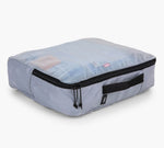Light gray packing cube with zipper and side handle, clear top showing folded clothes