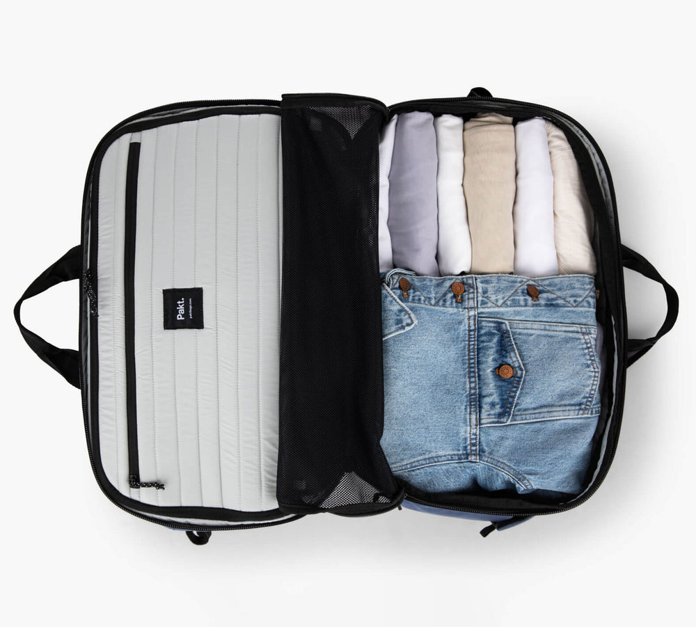 Open carry-on suitcase with folded shirts and a pair of jeans; gray zippered compartment on the left.