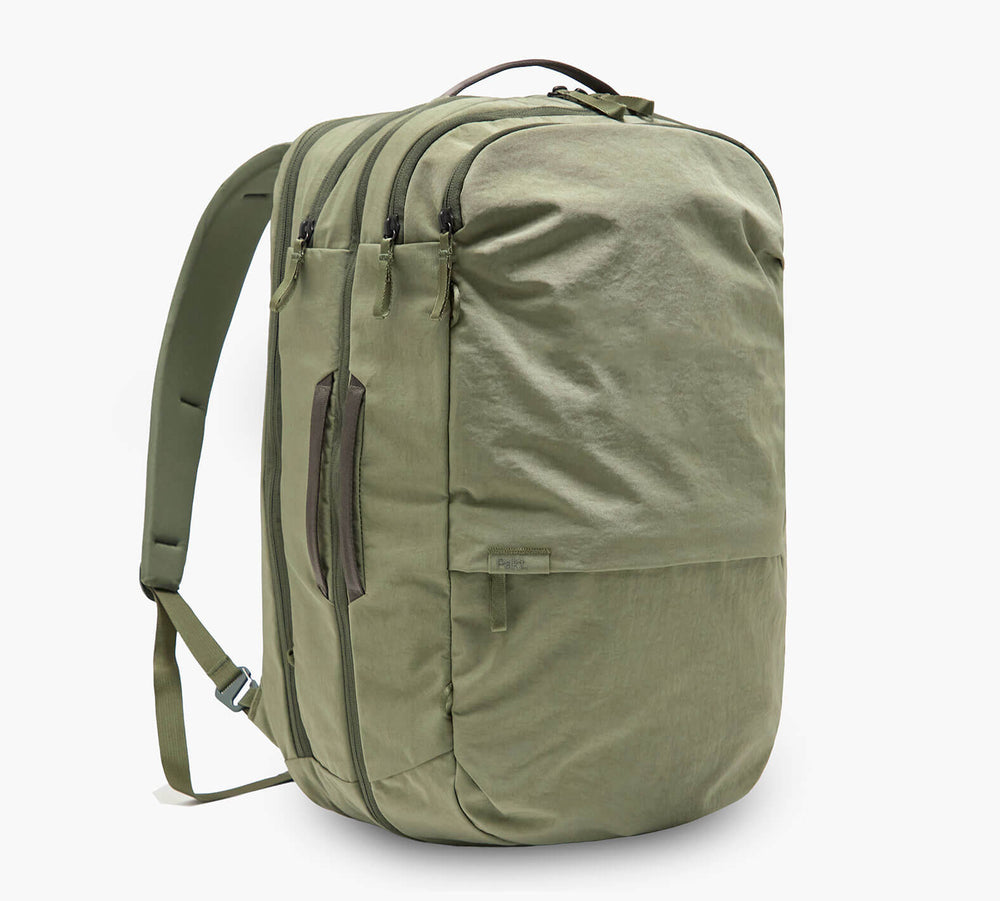 Three-quarter view of Pakt One Travel Backpack in cypress showing three zip compartments, side carry handle, and padded shoulder straps on white background