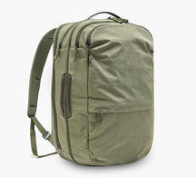 Three-quarter view of Pakt One Travel Backpack in cypress showing three zip compartments, side carry handle, and padded shoulder straps on white background