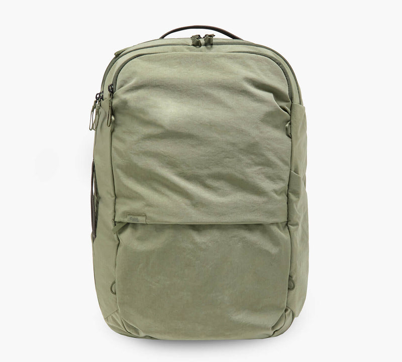 Olive-green canvas backpack with top handle, front zip pocket, and dual zippers.