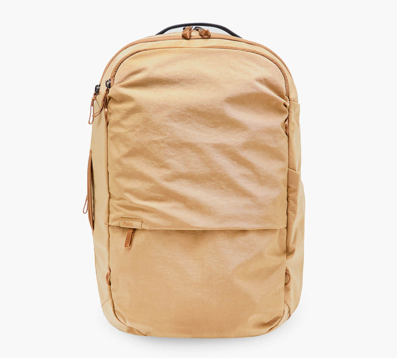 Tan canvas backpack with front zip pocket, top carry handle, and streamlined silhouette.