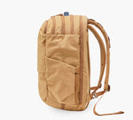 Tan canvas daypack with front pocket, vertical stitch detailing, and padded shoulder straps, shown from side.