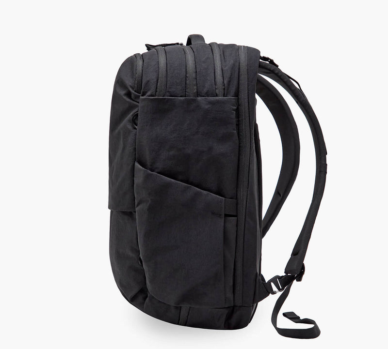 Black commuter backpack side view with angled exterior pocket and padded shoulder straps.