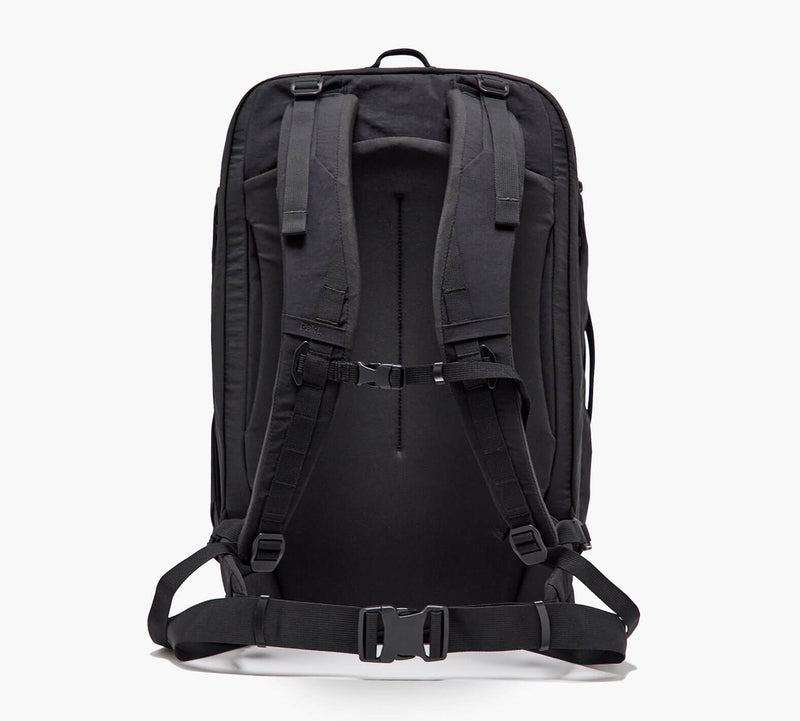 Black technical backpack viewed from the back with padded shoulder straps, sternum strap, and hip belt.