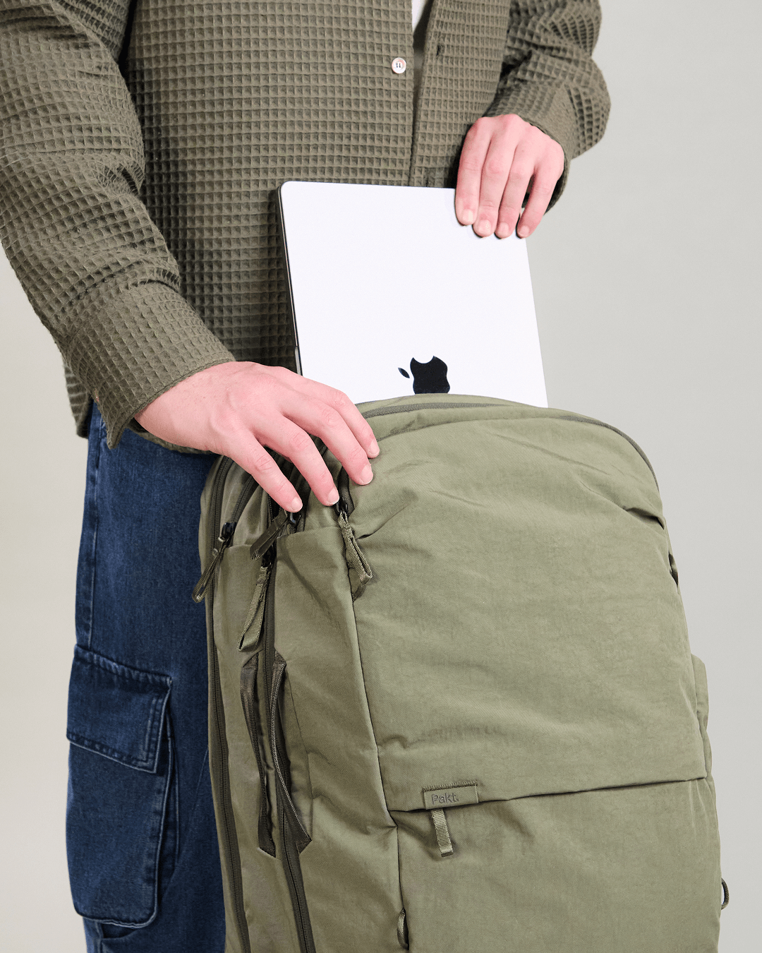 Front view of Pakt One Travel Backpack in cypress showing a person placing a laptop into the padded 16-inch laptop pocket