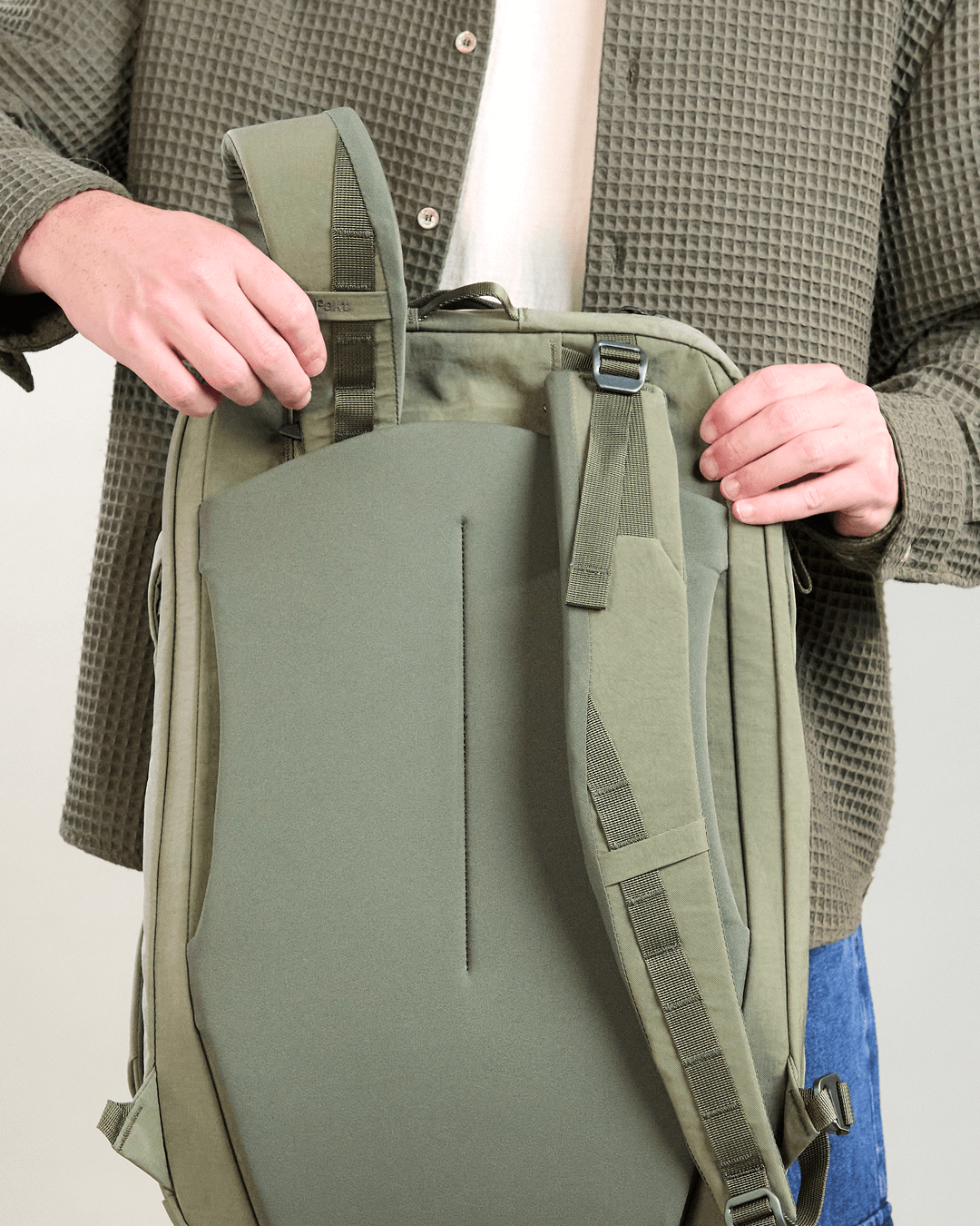 Rear view of Pakt One Travel Backpack in cypress showing stowable shoulder straps and padded back