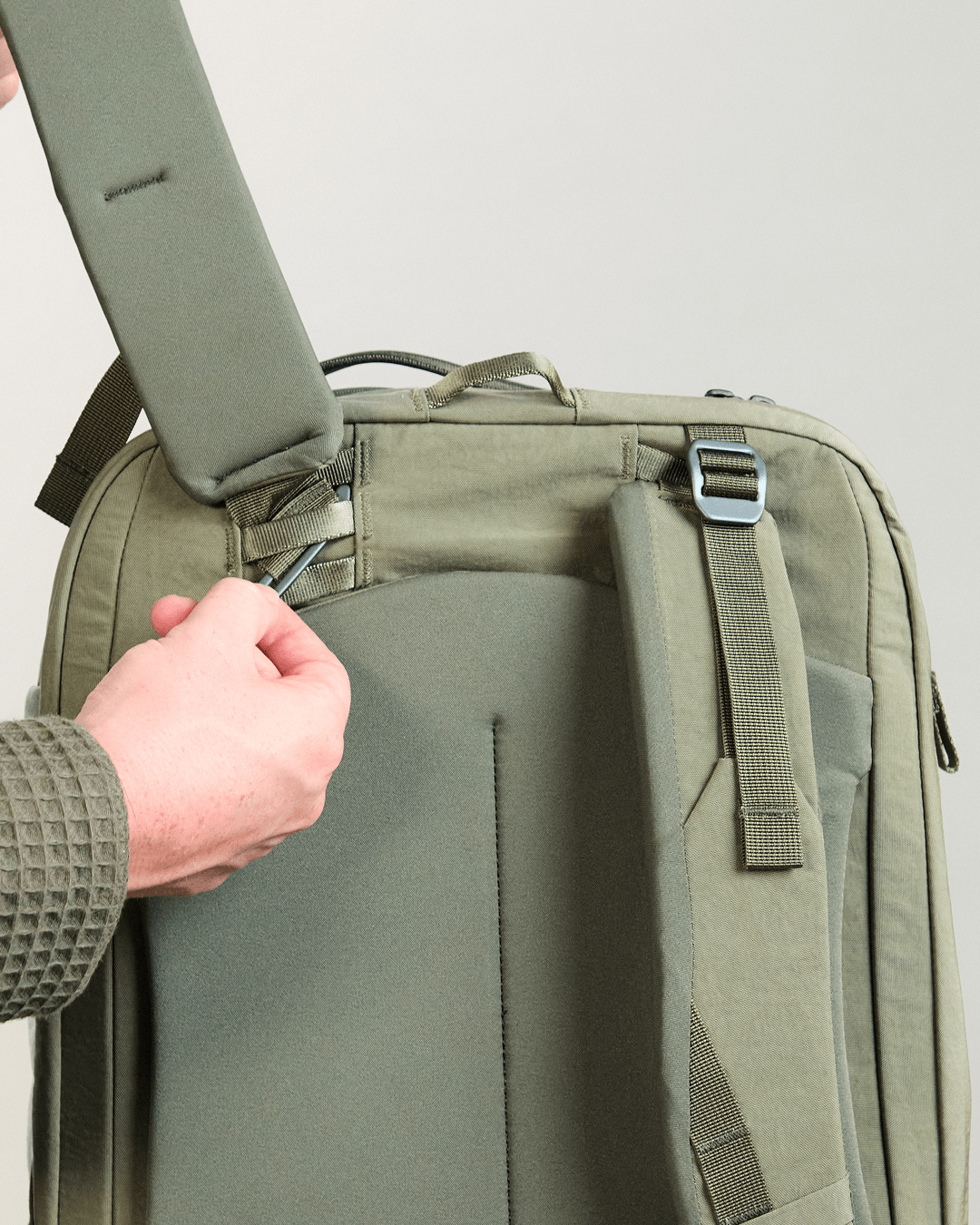 Rear of Pakt One Travel Backpack in cypress showing a shoulder strap being tucked into the padded back panel