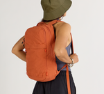 Back view of person wearing a rust-orange backpack and olive-green bucket hat against a plain background