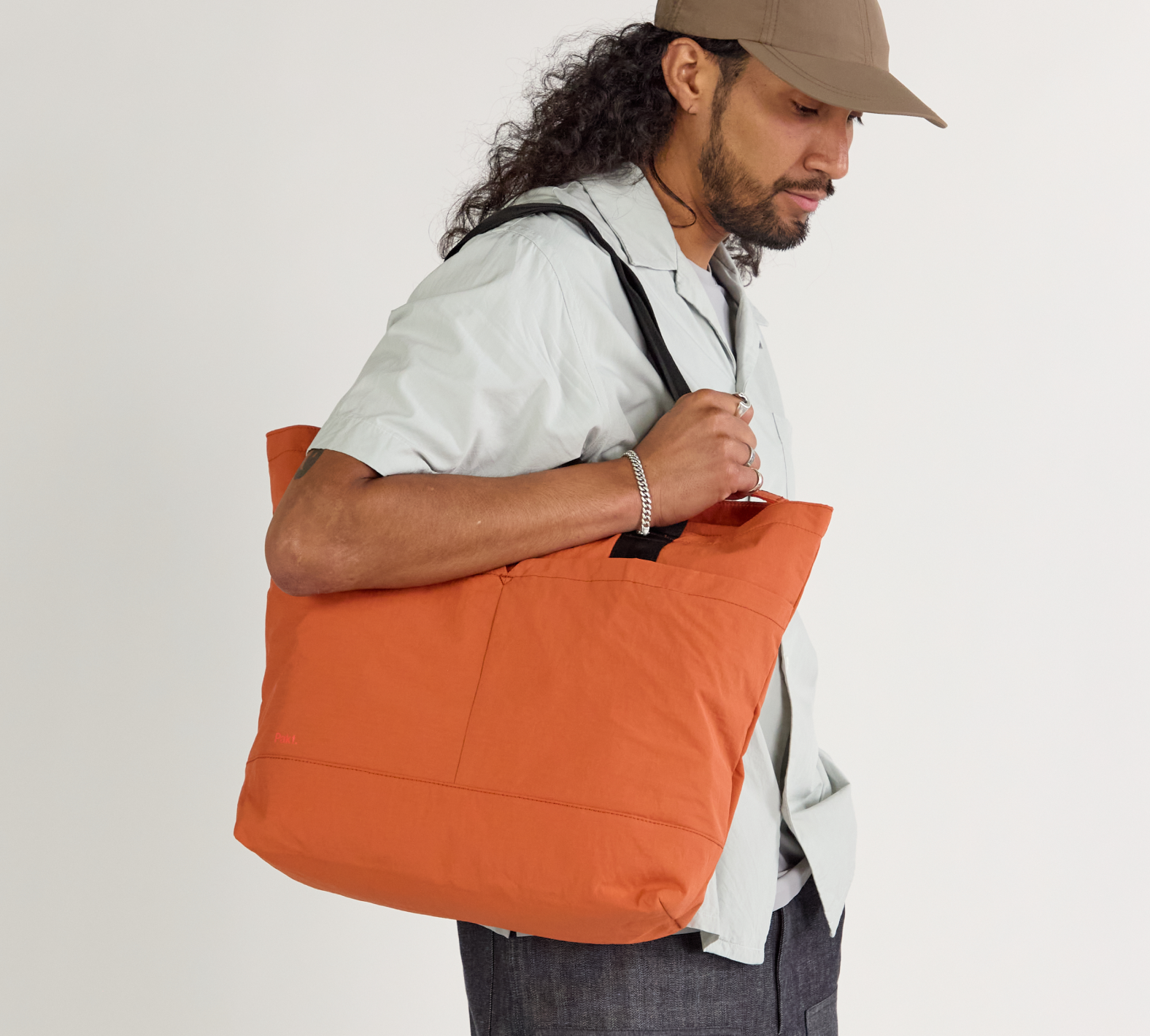 Side view of Stash Packable Tote in Sumac carried on a model's shoulder showing black straps and roomy zippered body