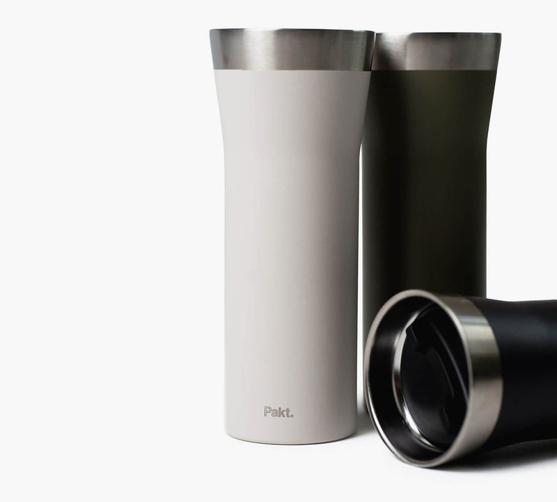 Three insulated travel tumblers—white, olive, and black with stainless rims; white tumbler reads 'Pakt.'