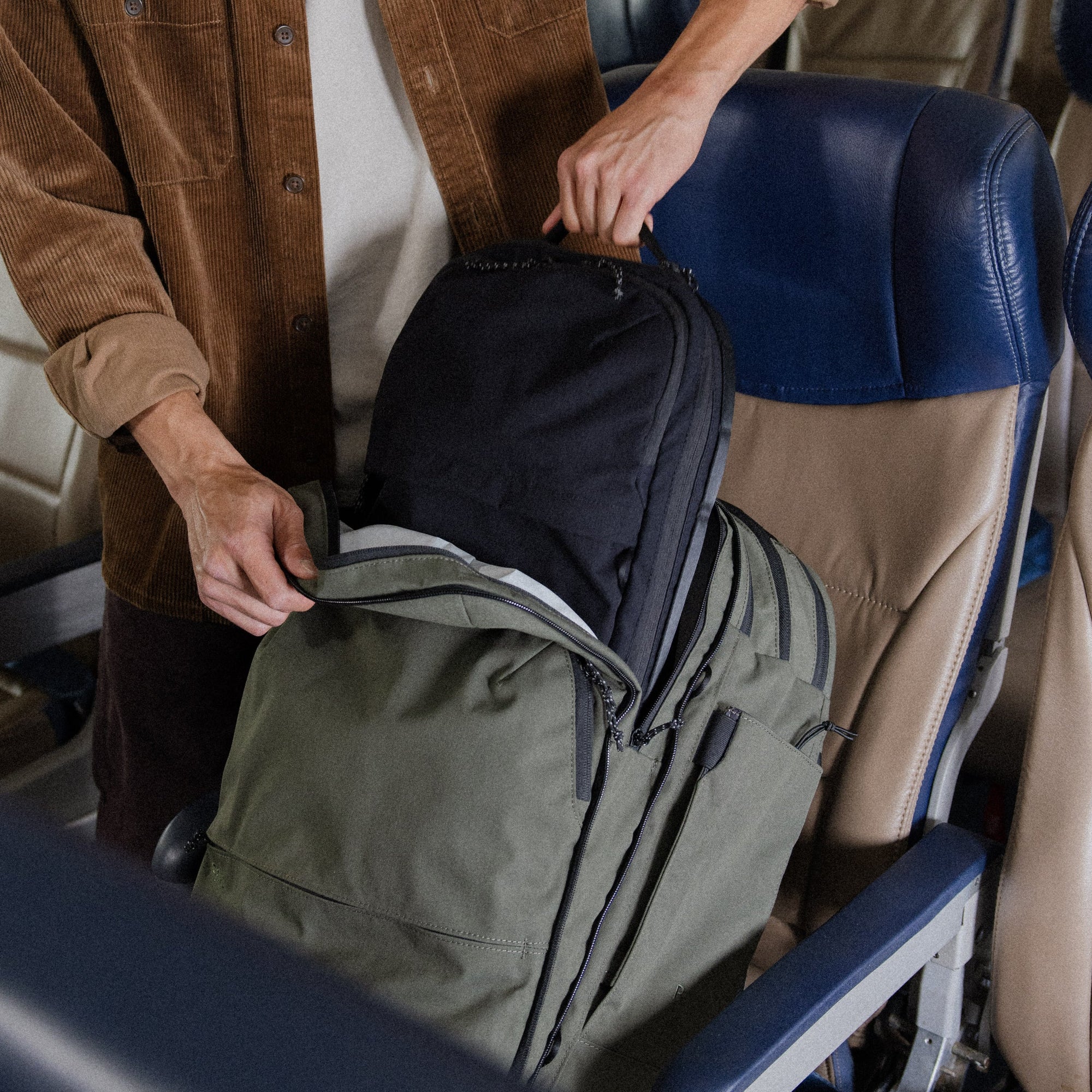 Traveler packing a cypress Pakt travel backpack on an airplane, placing a black pouch into the main compartment