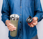 Person in denim shirt holding an open green stainless travel mug showing its metal interior and the black lid with red seal.
