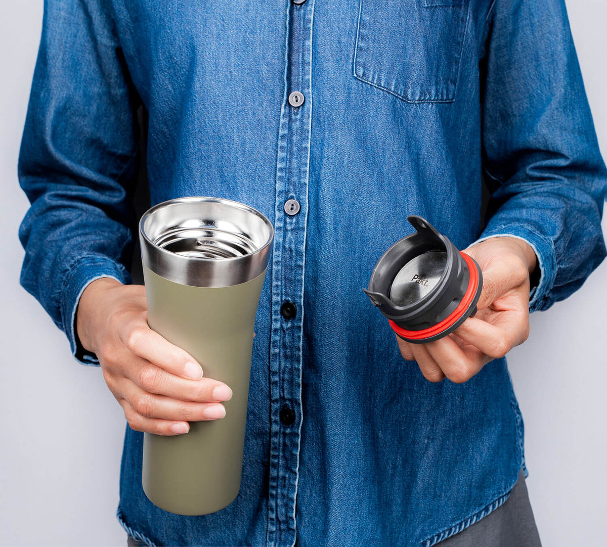 Person in denim shirt holding an open green stainless travel mug showing its metal interior and the black lid with red seal.