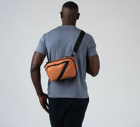 The Pakt 5L Sling in Adobe on the back of a male model